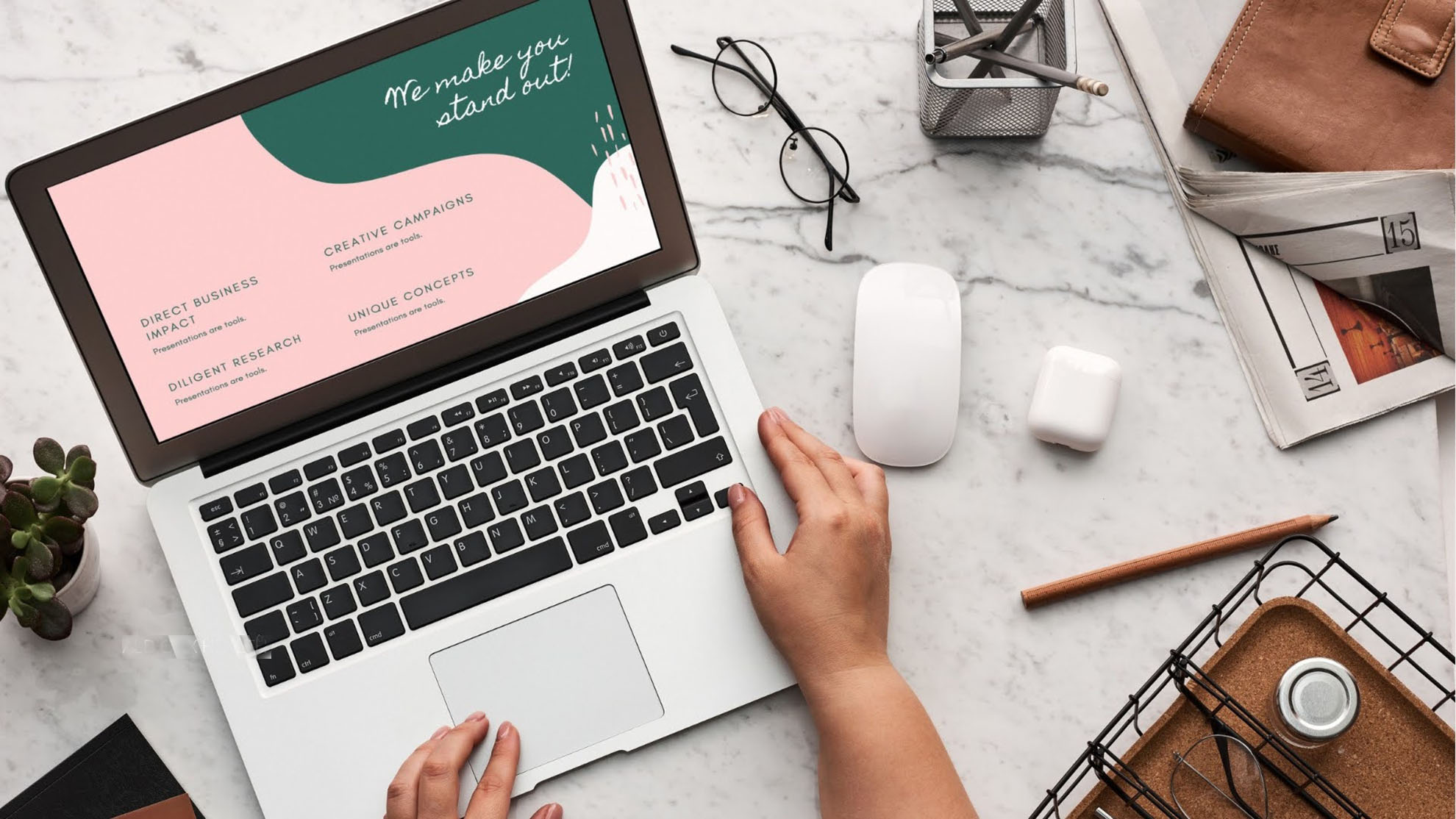 A woman is sitting at her desk facing her laptop. She is working on design of a website.  It is a marble top desk with a pair of reading glasses, pencils, office items on top. The website says Direct business impact, Creative campaigns and We make you stand out. 